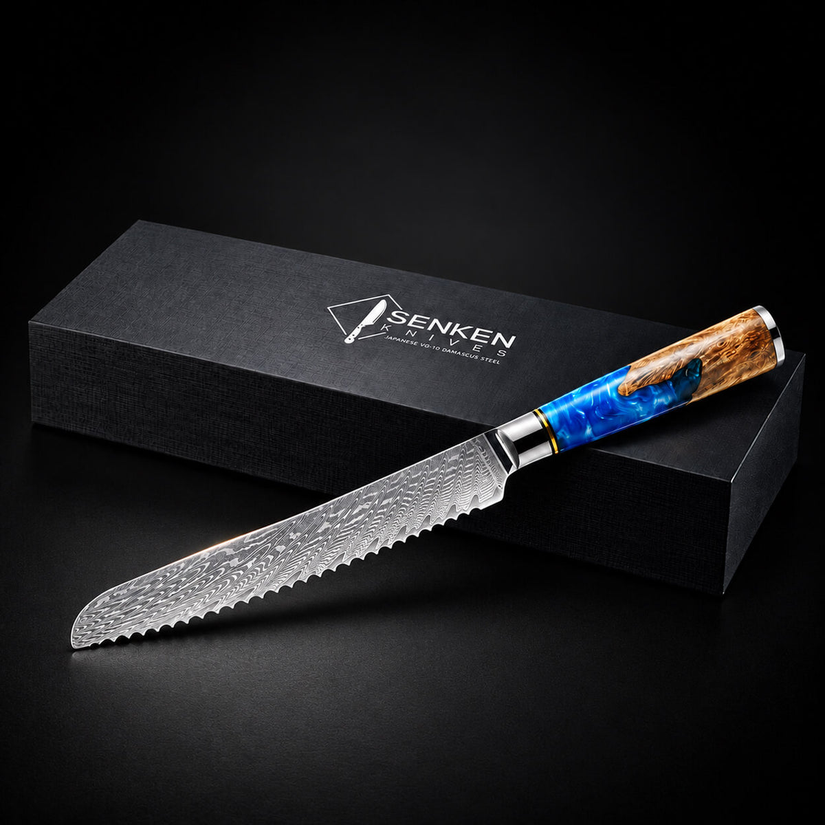 A serrated kitchen knife with a patterned Damascus-style steel blade and a blue marbled handle with a wood-grain end, displayed diagonally in front of a black SENKEN brand box on a dark background.