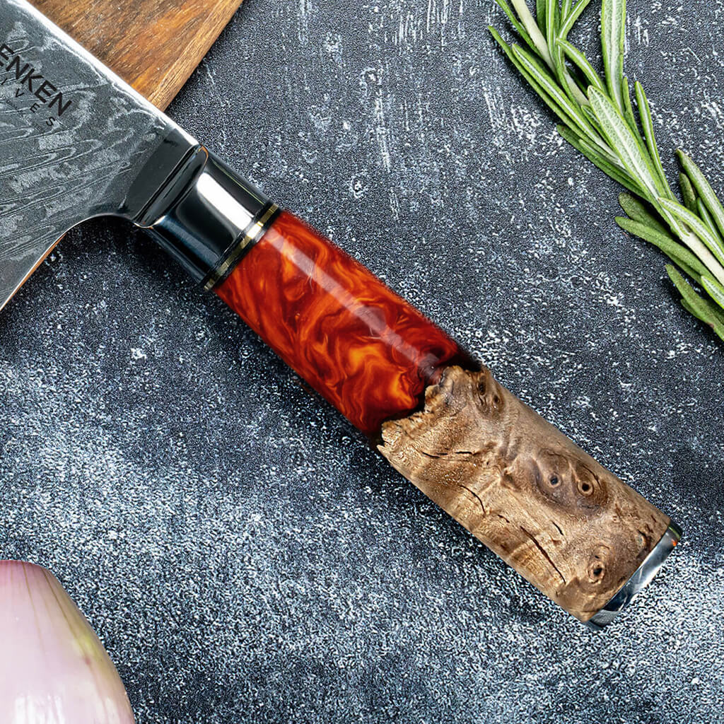 Senken Tsunami Damascus chef knife close-up showing red resin and burl wood handle with layered steel blade on stone surface with fresh rosemary