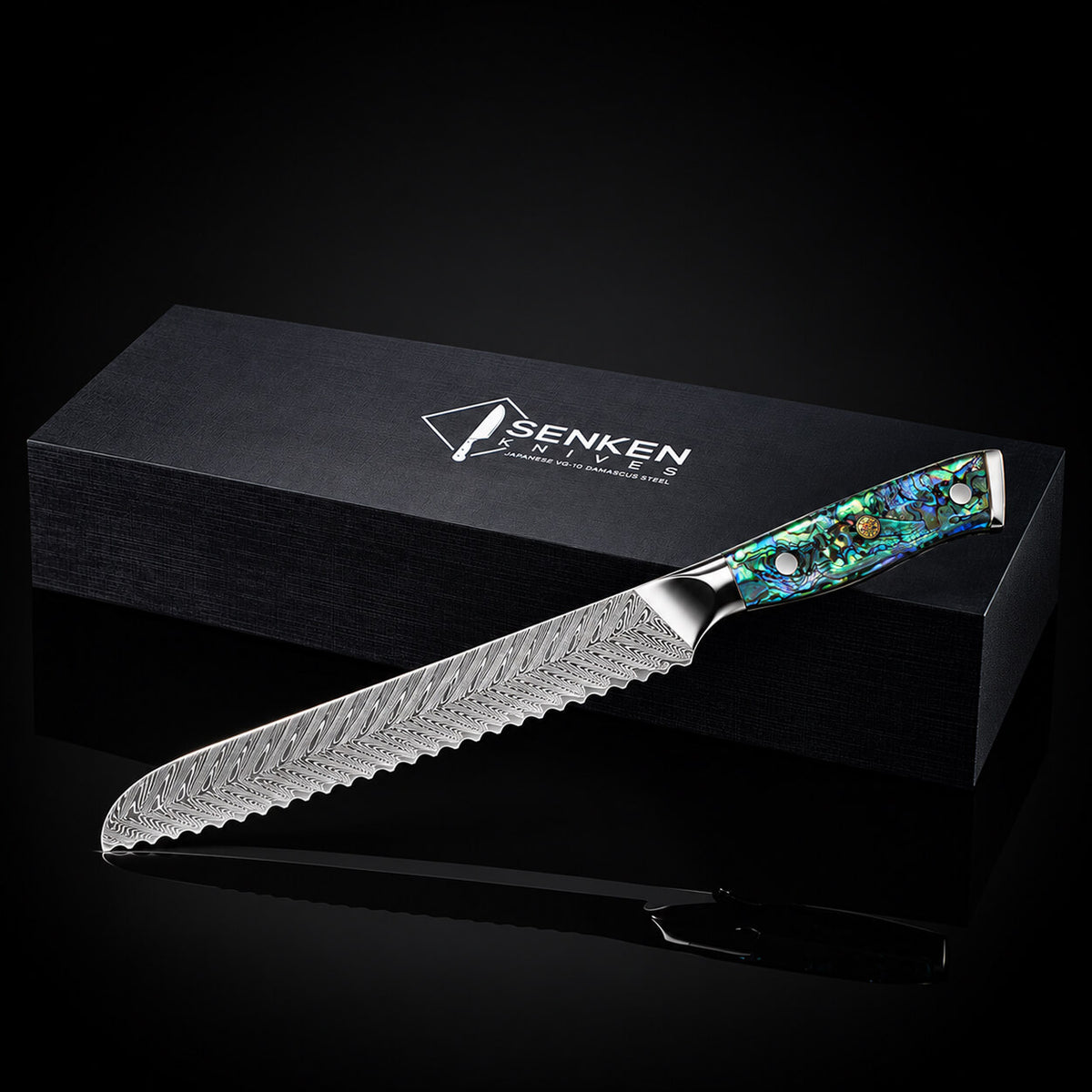 A Senken brand serrated bread knife with a patterned steel blade and a colorful iridescent handle, displayed diagonally in front of its black branded box on a reflective black surface.
