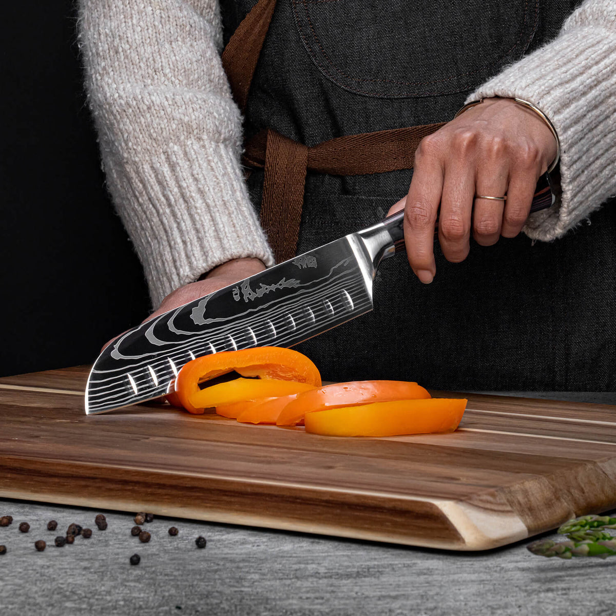 Person using a chef's knife to slice orange bell peppers on a wooden cutting board.