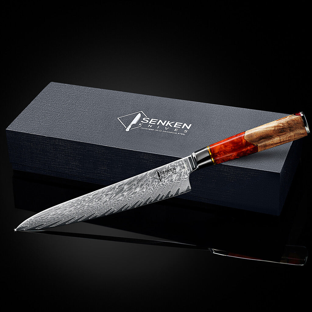 Senken Tsunami Damascus chef knife with patterned steel blade and red resin burl wood handle displayed in front of branded Senken Knives gift box on black background
